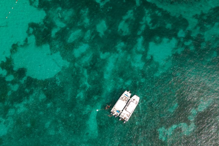 Aerial view of two boats on clear turquoise water near coral reefs.