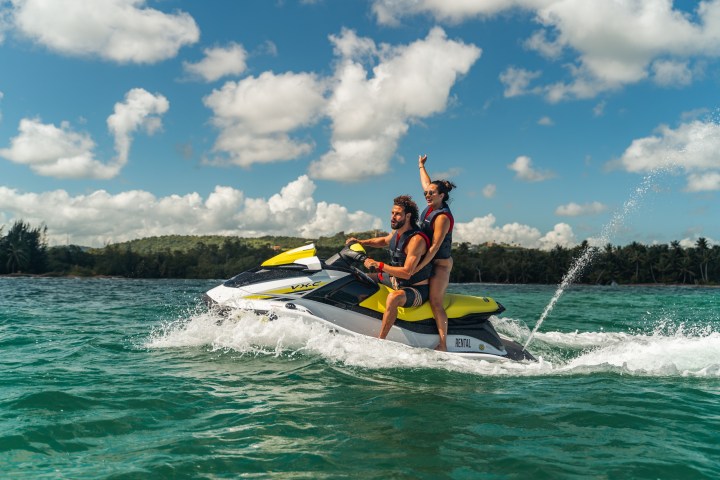 Two people riding a jet ski on blue water under a cloudy sky.