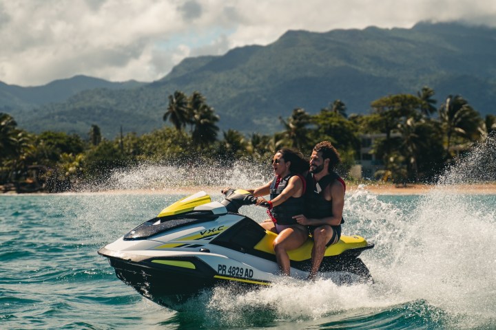 Two people riding a jet ski on a sunny day with mountains in the background.