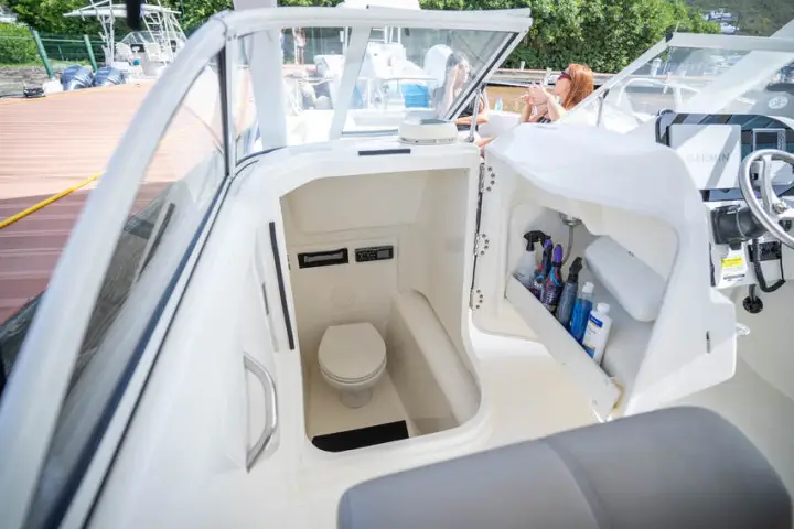 Boat’s small cabin with a toilet, cleaning supplies, and open side door.