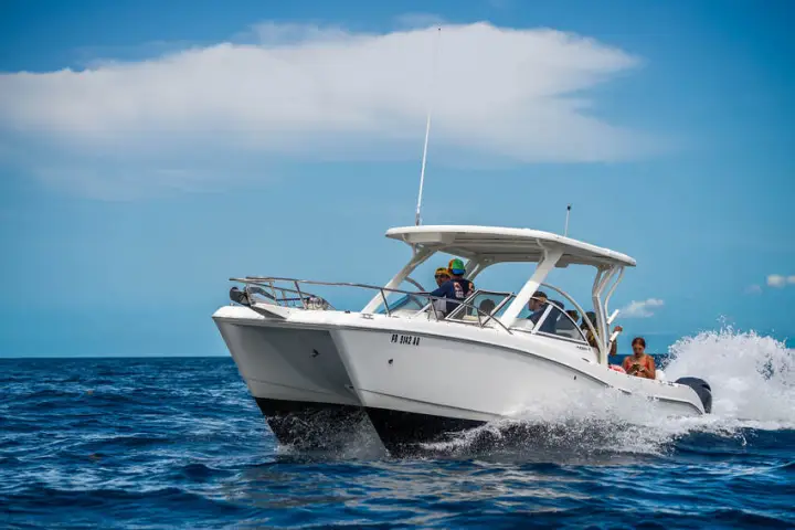 White motorboat with people speeding on the ocean under a blue sky.