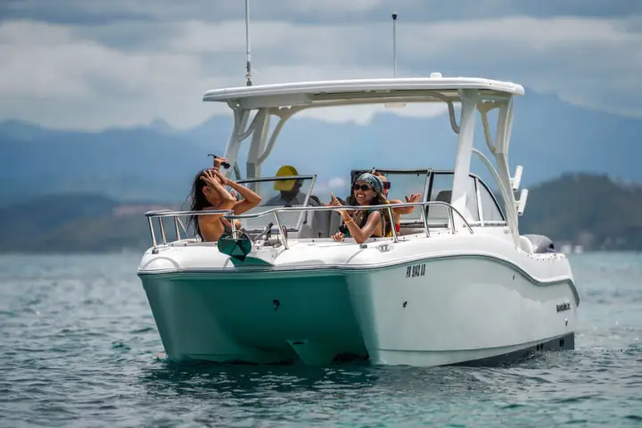 Two people relaxing on a motorboat in the ocean with mountains in the background.