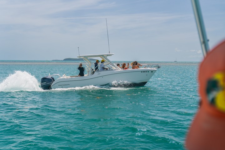 Speedboat on turquoise water viewed from another boat with a person in foreground.