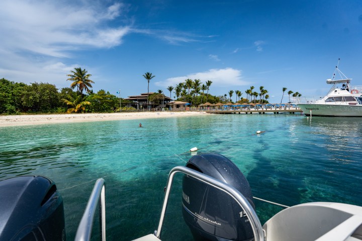 Tropical beach with palm trees and boats on clear blue water.